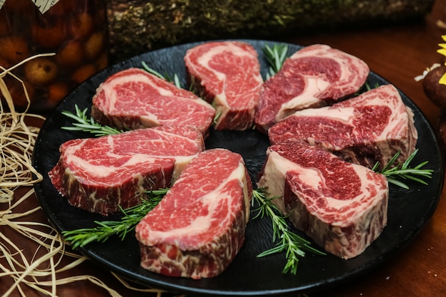 Front view raw marbled meat for steak with rosemary on a stand