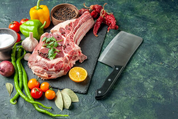 Front view raw meat slice with fresh vegetables salt and pepper on dark blue surface