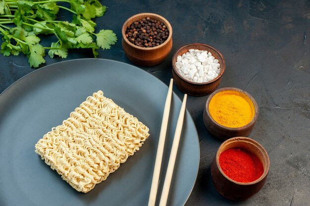 Front view raw noodles inside plate with seasonings on dark-blue table