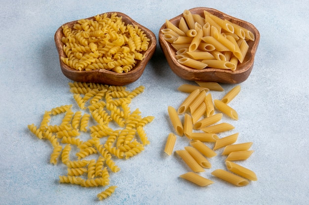 Vista frontale della pasta cruda in ciotole su una superficie grigia