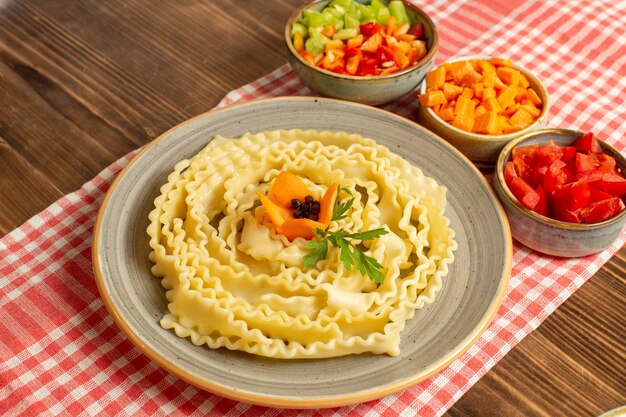 Front view raw pasta dough with sliced vegetables on brown space