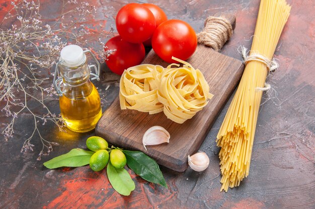 Front view raw pasta with oil tomatoes and garlic on dark surface raw pasta dough