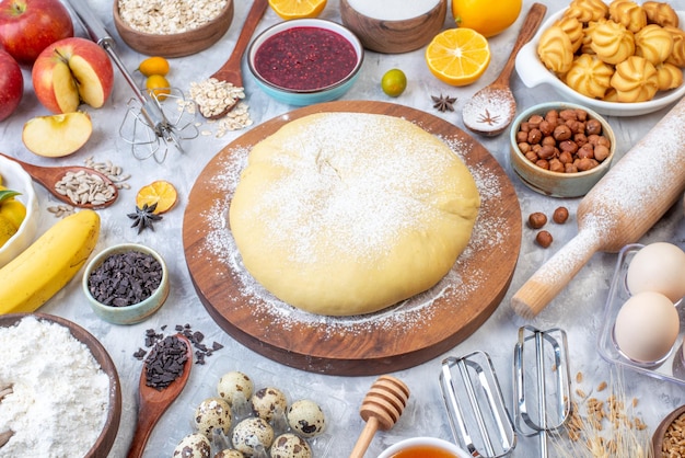 Free photo front view of raw pastry flour on round board grater fresh fruits jam cookies hazelnuts on stained white background