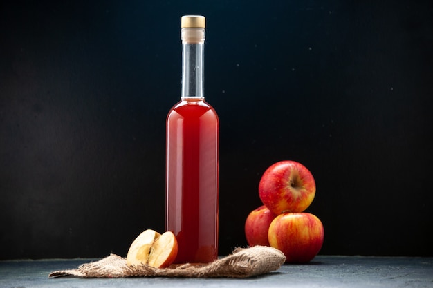 Красный яблочный соус в бутылке со свежими яблоками на темной поверхности, вид спереди