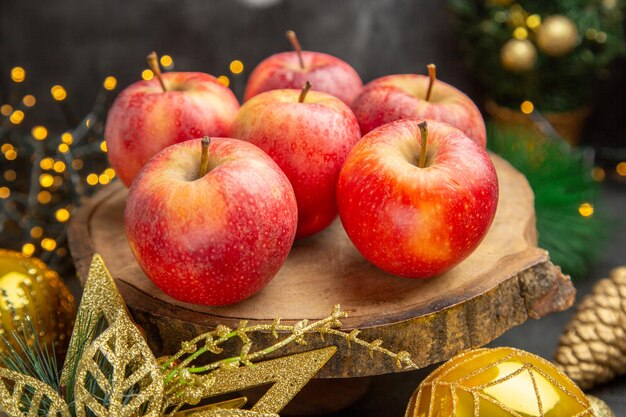 暗い背景の上のクリスマスのおもちゃの周りの正面の赤いリンゴ