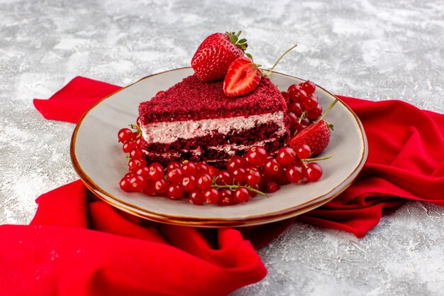 Front view red cake slice fruit cake piece inside plate with fresh cranberries and strawberries alogn with red tissue on grey