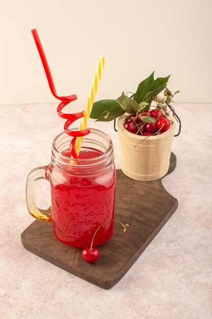 Коктейль из красной вишни с соломкой и вишней на розовом столе, вид спереди, фруктовый напиток, сок