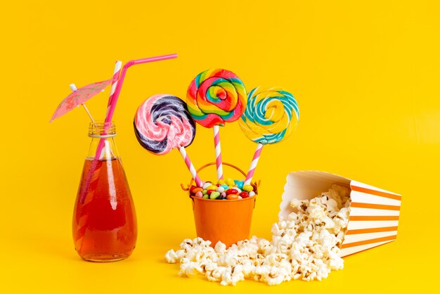 A front view red cocktail cooling with straw alogn with colorful candies lollipops and popcorn on yellow