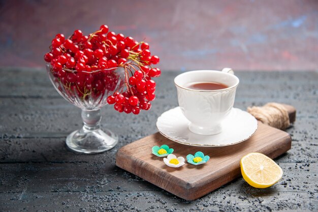 正面図赤スグリのグラスにチョッピングボードにお茶を一杯、暗い背景にレモンのスライス