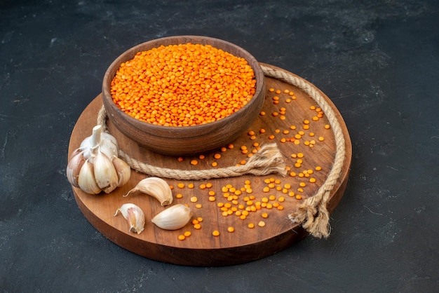 Free photo front view of red lentil in a brown bowl rope garlics on wooden round board on black background