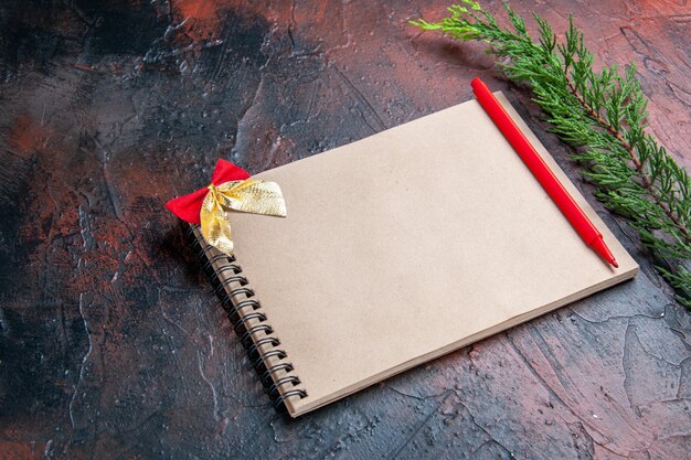 Front view red pen a notepad with little bow a pine tree branch on dark red background