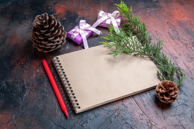 Front view red pen a notepad xmas gifts pinecones a pine tree branch on dark red background