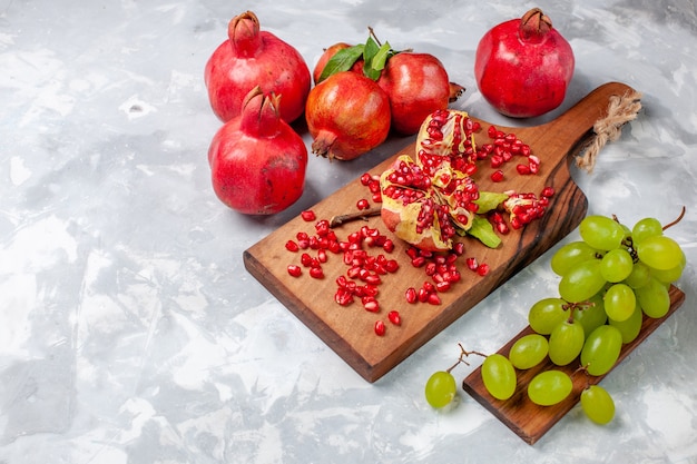 Frutti freschi e succosi del melograno rosso di vista frontale con l'uva sullo scrittorio bianco