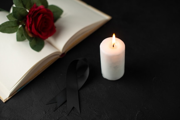 Front view of red rose with open book and candle on black