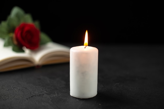 Front view of red rose with open book and candle on black