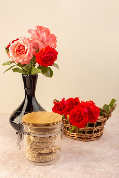 A front view red roses beautiful pink and red flowers inside black jug along with crisps isolated on pink