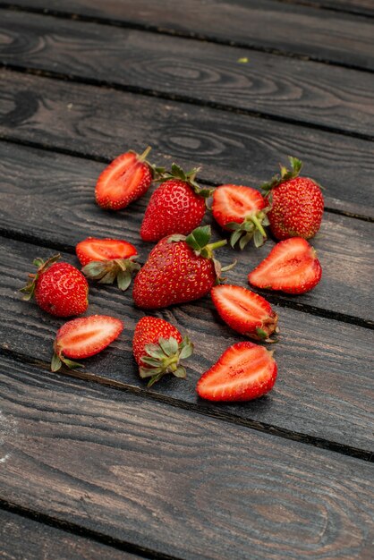 Front view red strawberries sliced and whole fruits on dark wooden rustic desk summer color wild tree juice berry