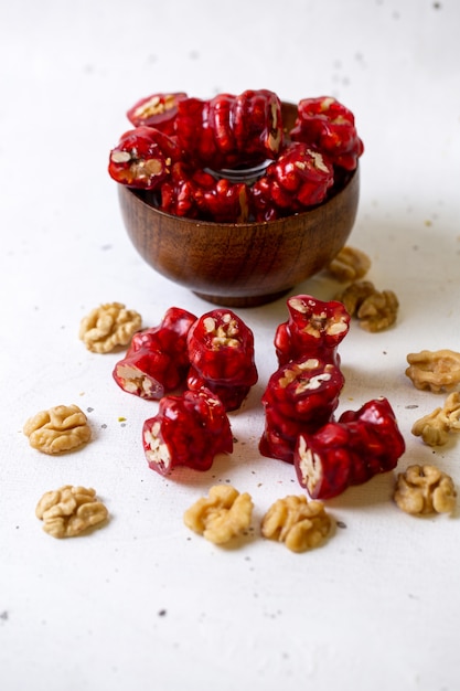 Вид спереди красные сладости внутри коричневой миски вместе с грецкими орехами на белом