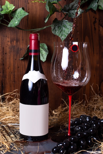 A front view red wine bottle of red wine along with black grapes and green leaves isolated on the grey desk alcohol winery drink