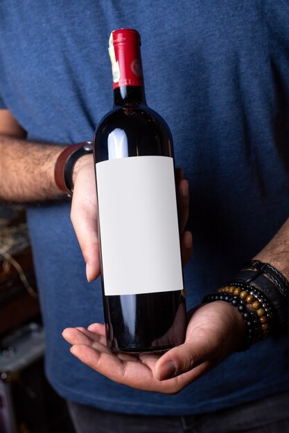 A front view red wine young man holding a bottle of red wine with red cap alcohol winery drink