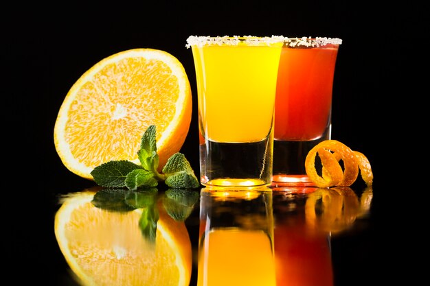 Front view of red and yellow cocktail in shot glasses with orange