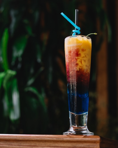Front view refreshing multi-colored cocktail with a blue straw