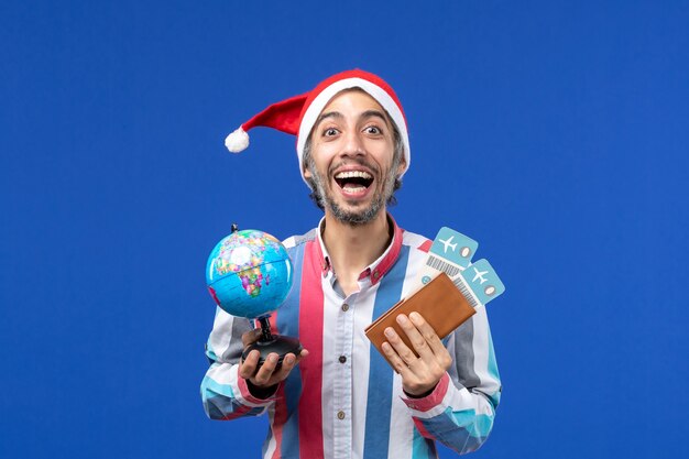 Front view regular male with tickets and globe on a blue wall color holiday new year