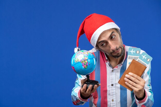青い壁の感情の休日の新年にチケットと地球儀を持つ通常の男性の正面図