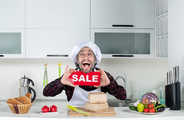 Front view of rejoiced male chef holding up sale sign in the kitchen