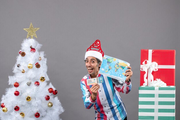 Front view rejoiced man with spiral spring santa hat holding map and travel ticket