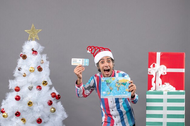 Front view rejoiced man with spiral spring santa hat holding world map and travel ticket