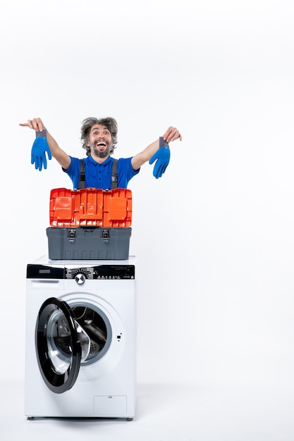 Free photo front view of rejoiced repairman holding gloves behind washing machine on white wall