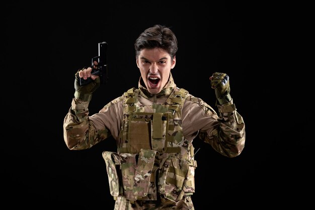 Вид спереди радующегося военнослужащего в форме с ружьем на черной стене