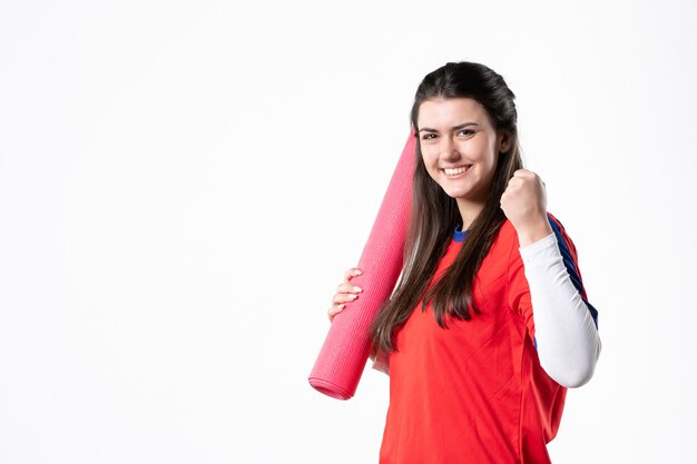Front view rejoicing young female in sport clothes with yoga mat