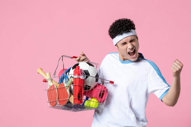 Front view rejoicing young male in sport clothes with basket full of sport things