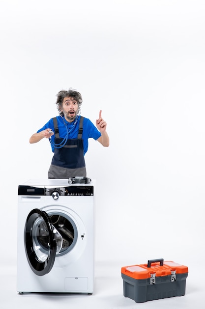 Front view of repairman holding stethoscope standing behind washer on white wall
