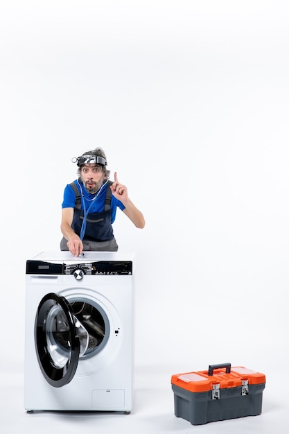 Free photo front view of repairman with head lamp putting stethoscope on washing machine on white wall