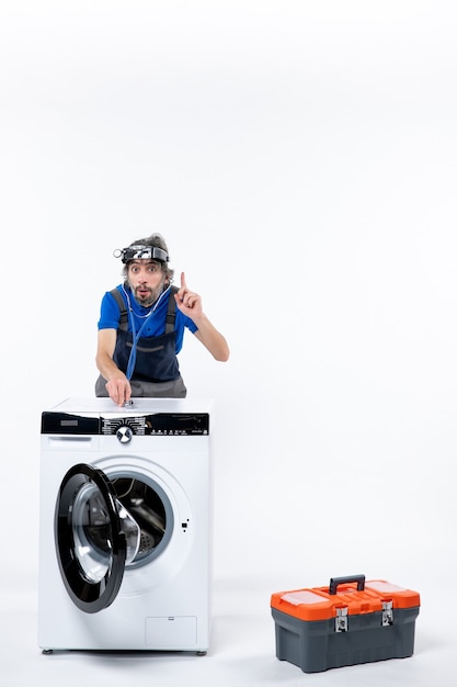 Front view of repairman with head lamp putting stethoscope on washing machine on white wall