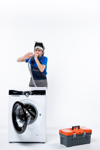 Front view of repairman with head lamp standing behind washing machine blowing out pipe on white wall