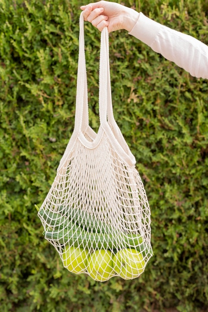 Front view reusable bag with groceries held by woman hand in nature