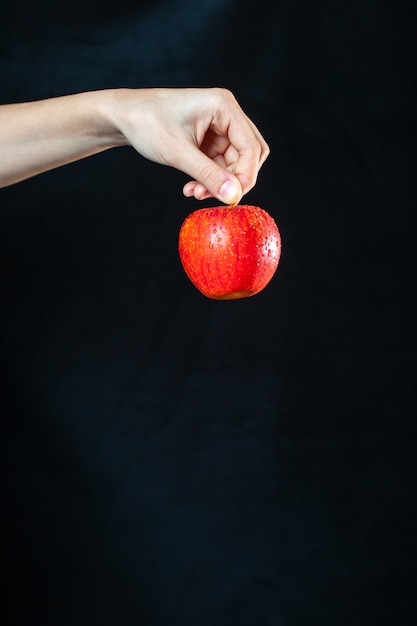 Вид спереди спелое красное яблоко в руке на темной поверхности