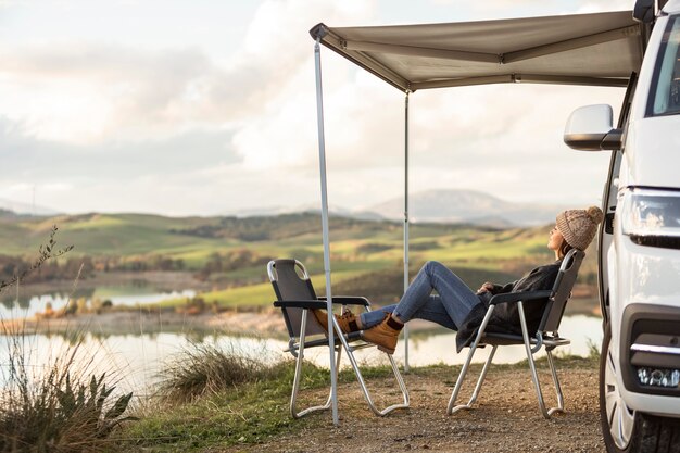 Front view of road trip car next to lake with woman relaxing