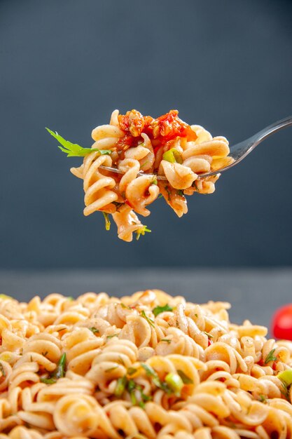 Front view rotini pasta on plate and on fork on dark isolated surface