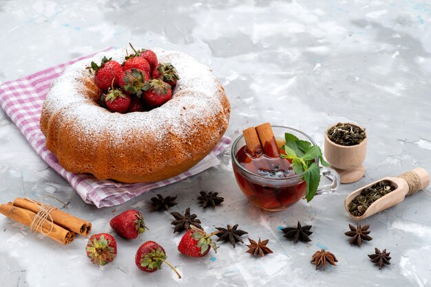 A front view round cake with sugar powder red strawberries tea on the white desk berry fruit cake 