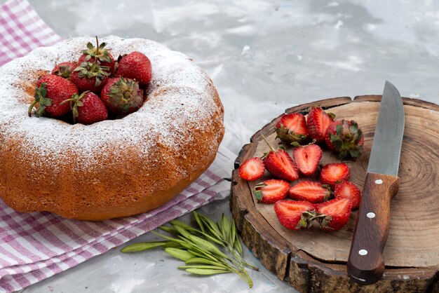 A front view round cake with sugar powder red strawberries on the white desk berry fruit cake 