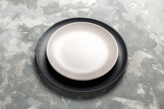 Вид спереди круглая пустая тарелка черного цвета с белой тарелкой на сером столе.