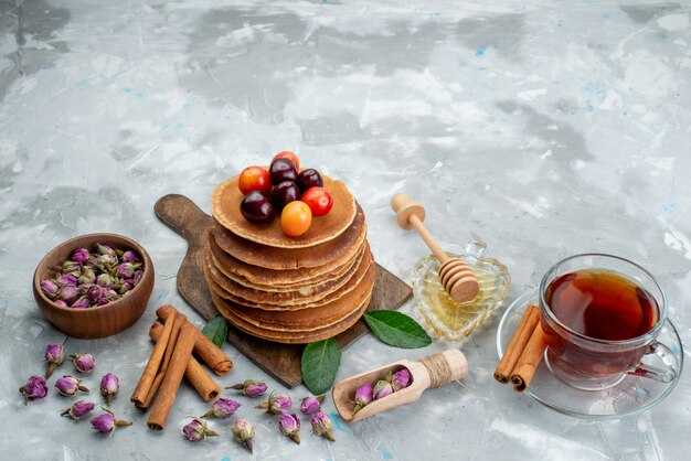 A front view round pancakes baked and delicious with cherries tea and cinnamon on the light desk cake fruit 