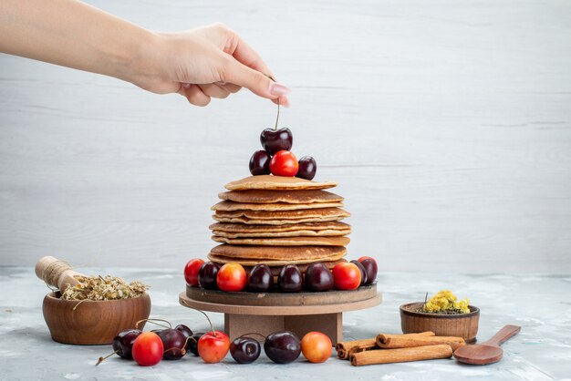 Free photo a front view round pancakes with cherries and cinnamon on the bright background cake fruit