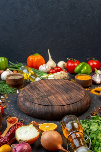 Front view round wooden board turmeric in small bowl green onions oil bottle green pepper tomatoes on table