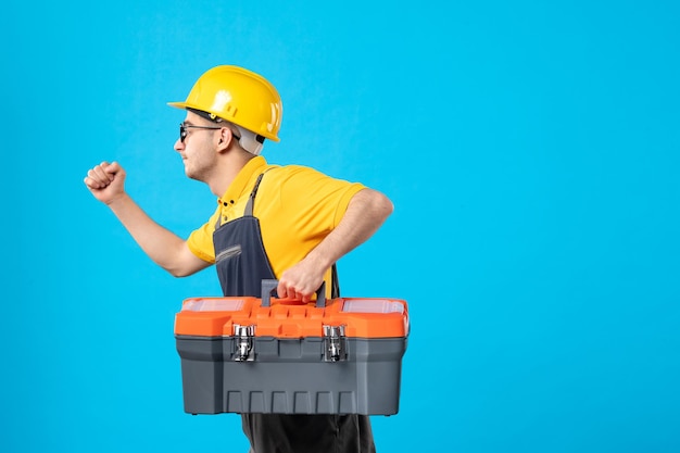 Free photo front view of running male builder in uniform with tool box in his hands on a blue